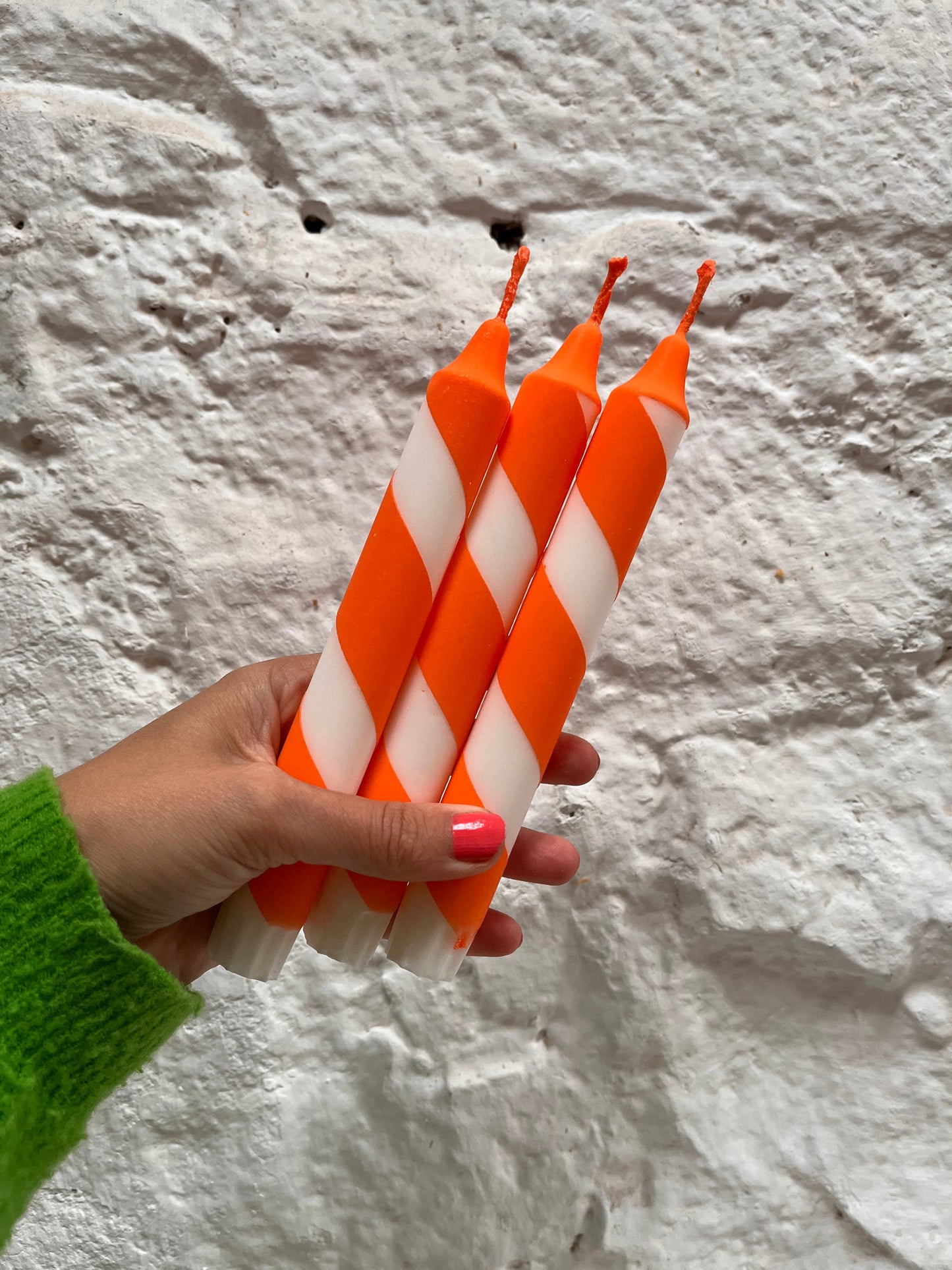 Hand holding three orange and white striped candles against a textured white background