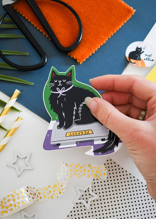 Hand holding a sticker of a cat on a craft table with scissors and fabric