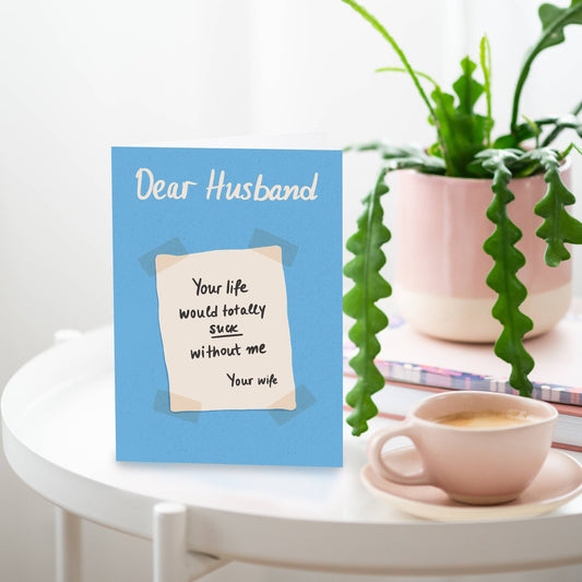 A blue greeting card with the text 'Dear Husband' at the top and 'Your life would totally suck without me - your wife' written in a humorous tone.