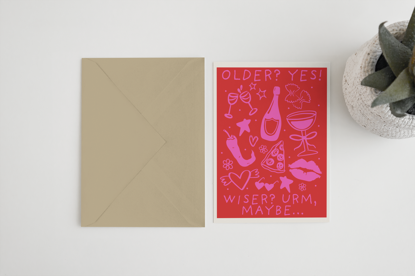 Pink birthday card with illustrations and beige envelope on a white surface