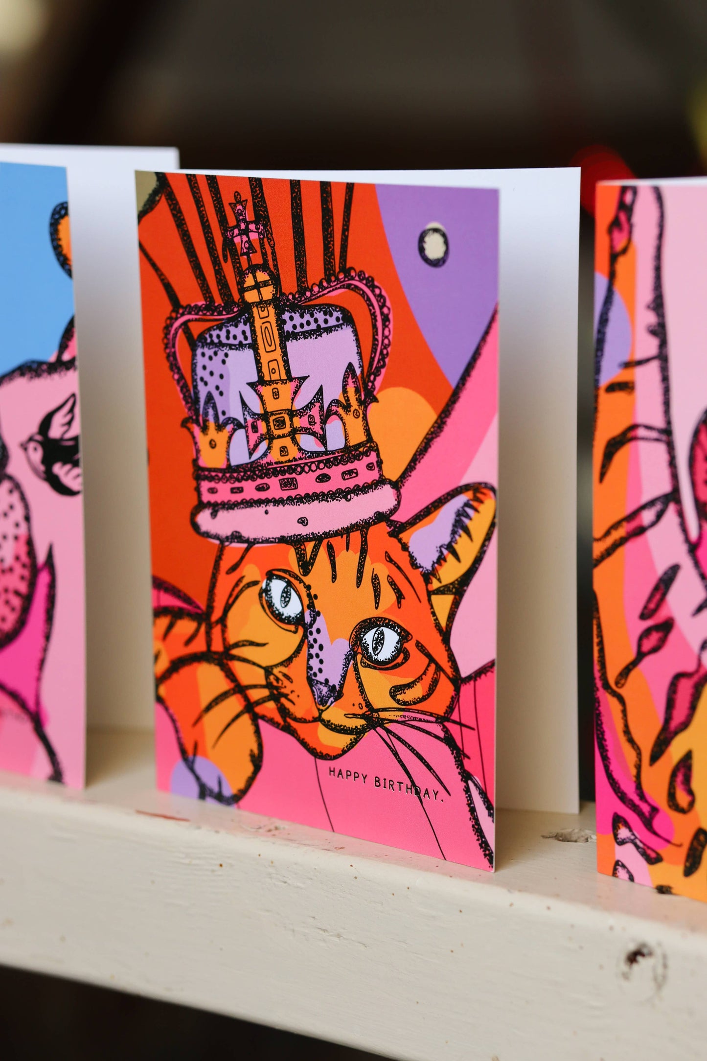 Ilustration of a cat wearing a crown in pinks, reds and oranges