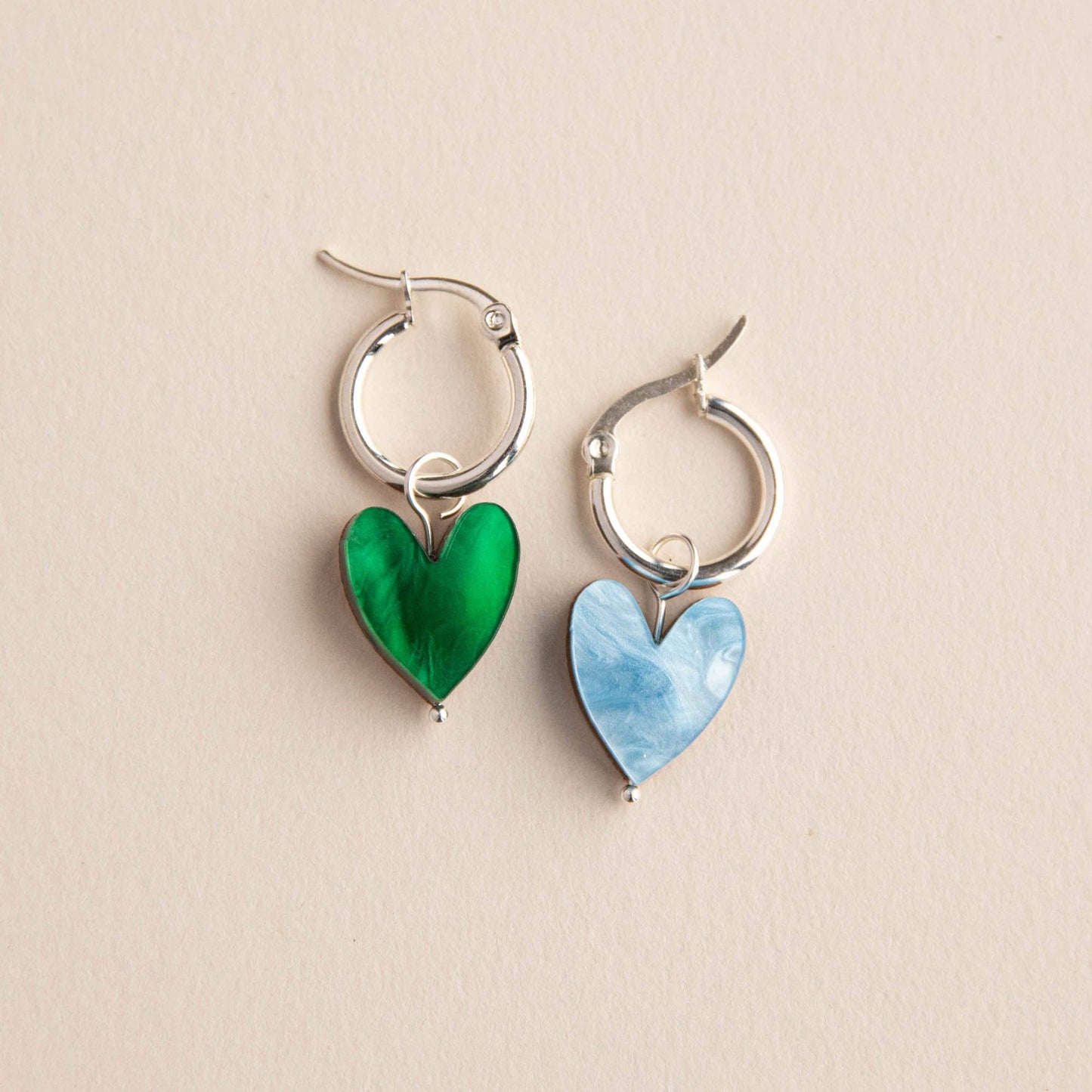 Pair of hoop earrings with green and blue heart-shaped charms on a beige background