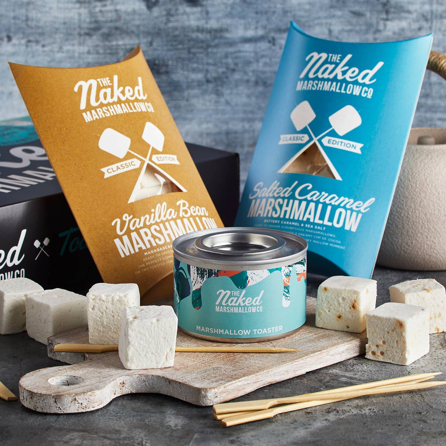 Naked Marshmallowco products including marshmallows, packaging, and a toaster on a gray surface.