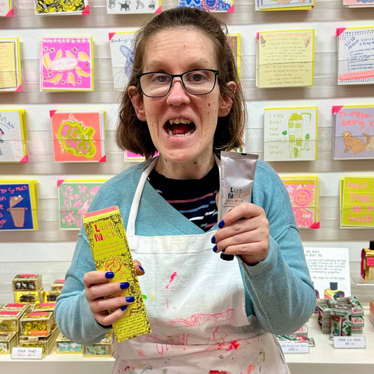 Person in a craft store holding a product with colorful cards and stationery in the background