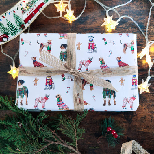 Gift wrapped in festive paper with Christmas-themed illustrations on a wooden surface with string lights.