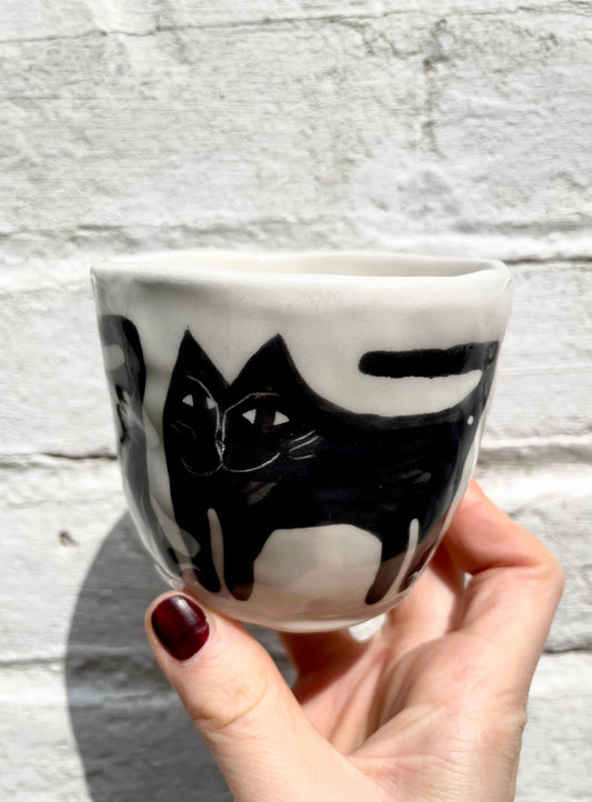 Ceramic cup with black cat design held by a hand against a light wooden background