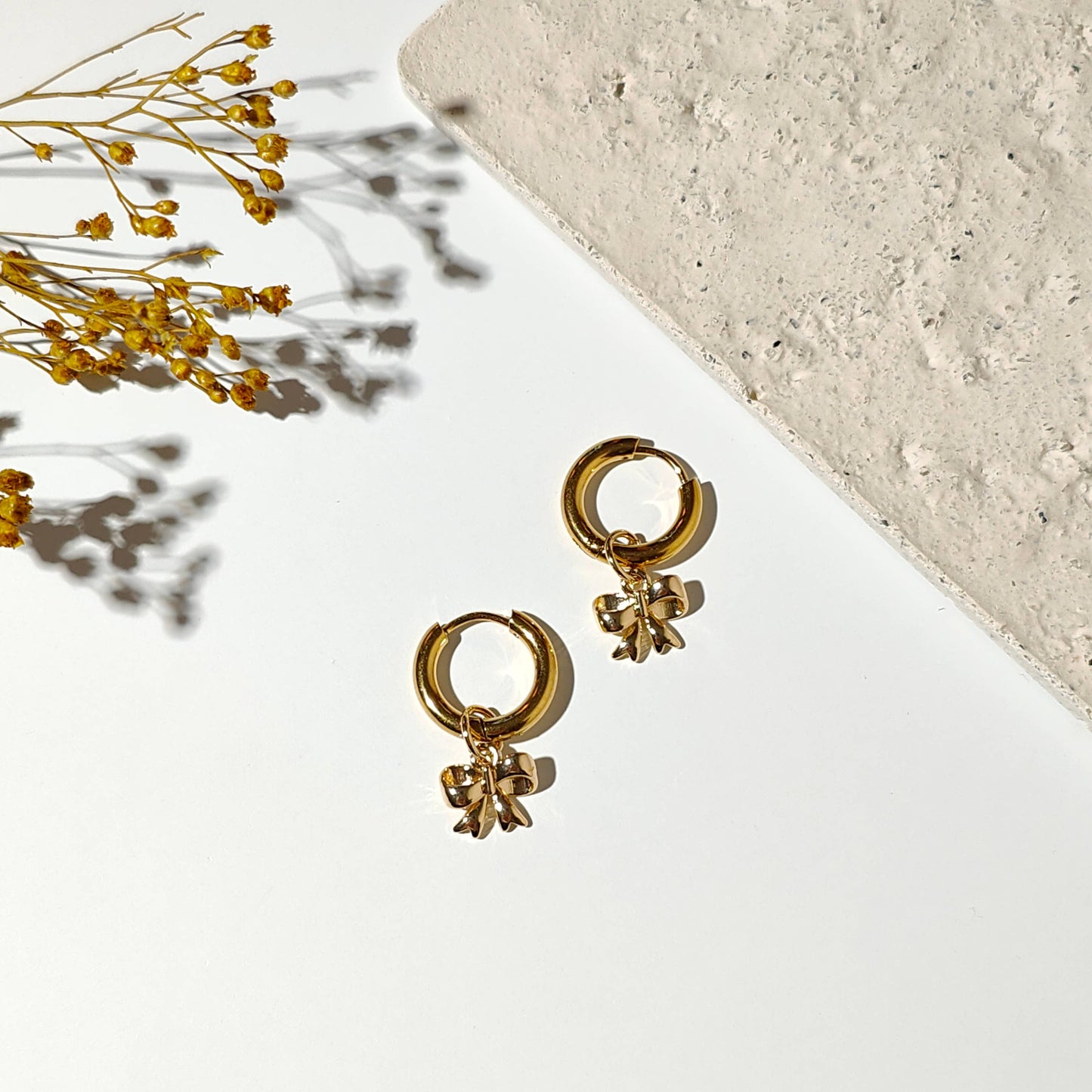 Gold plated hoop earrings with a bowtie ribbon charm