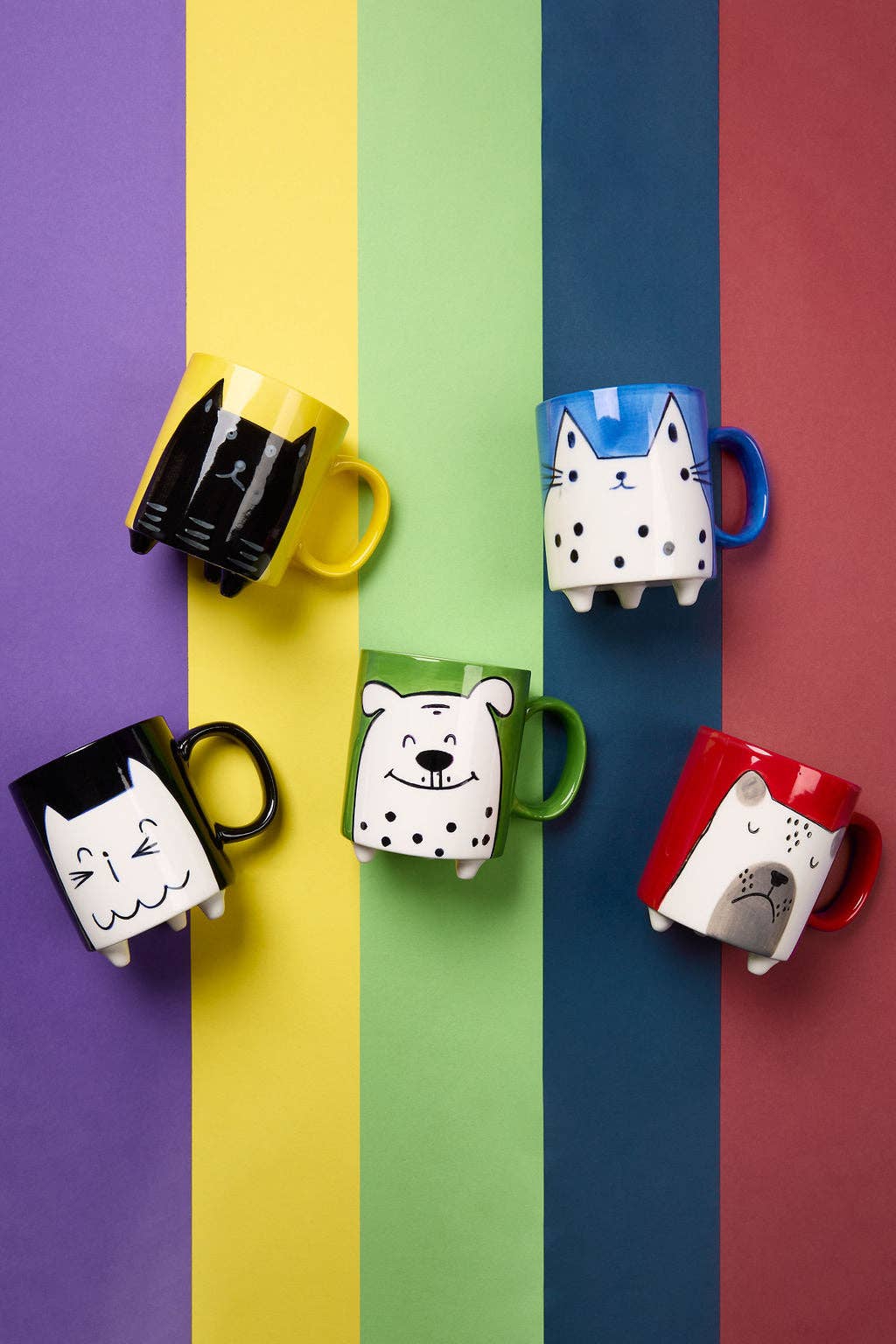 Colorful mugs with cat designs on a multicolored striped background