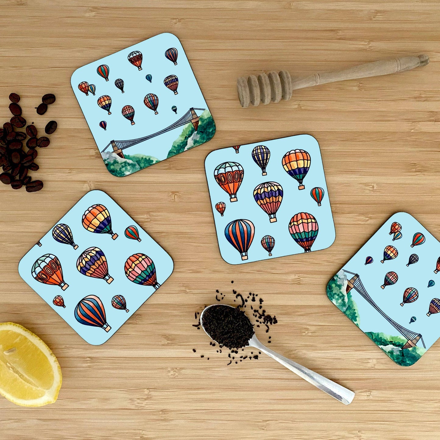 Four coasters with hot air balloon design on a wooden surface with coffee beans and a spoon.
