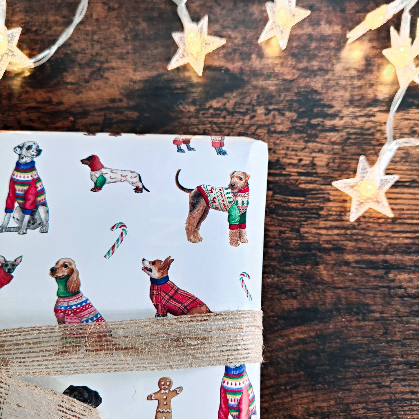 Gift wrap with dog illustrations on a wooden surface with string lights.