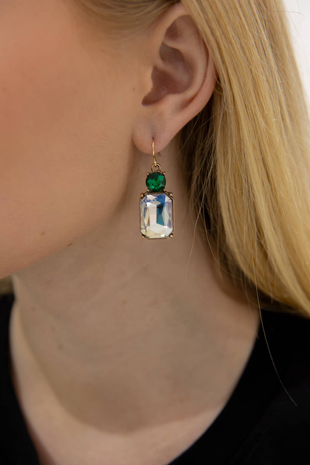 Close-up of a person wearing an earring with a green gemstone and clear crystal.