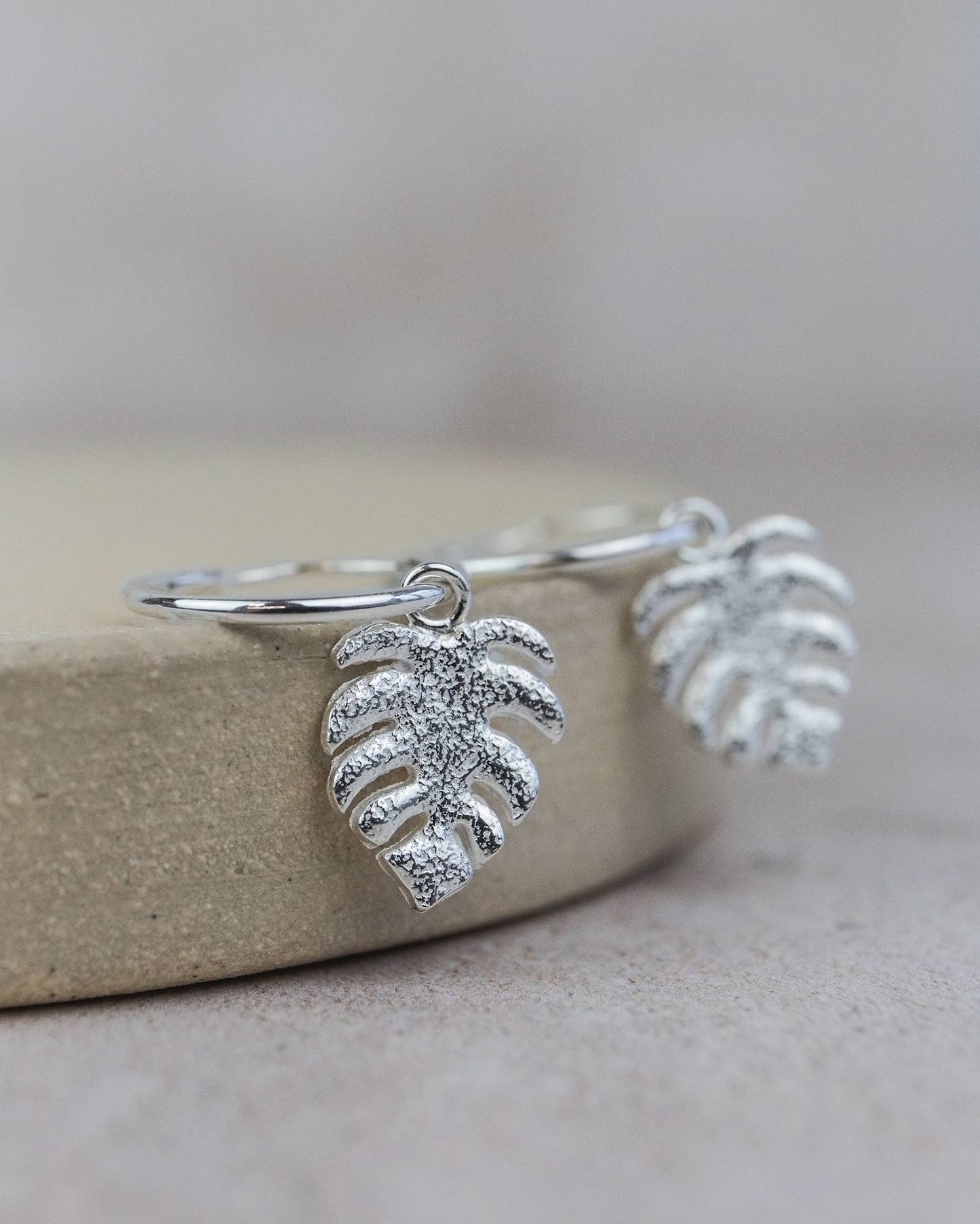 Silver leaf-shaped earrings on a beige stone surface