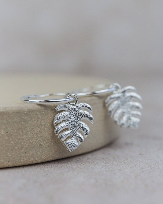 Silver leaf-shaped earrings on a beige stone surface