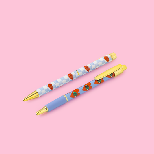 Two decorative pens with a checkered pattern and red heart designs on a pink background