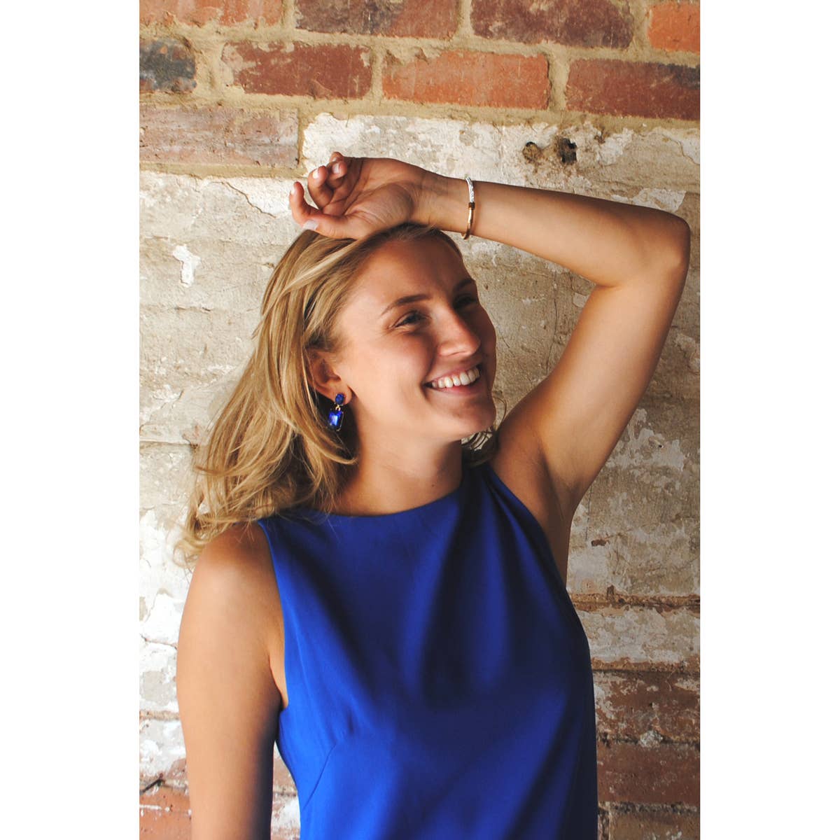 Woman in a blue dress posing against a brick wall
