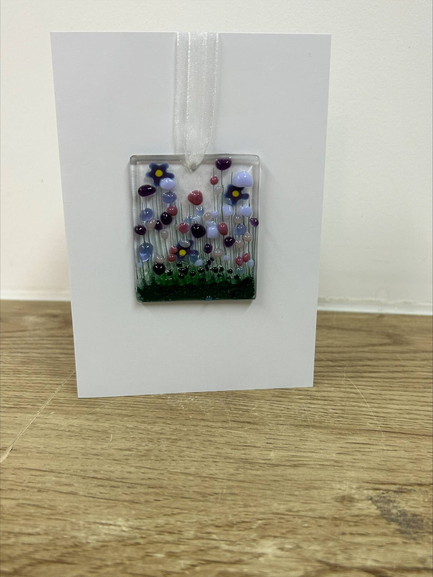 Decorative glass panel with flowers on a white card against a wooden surface