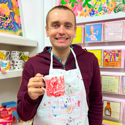 Man holding a mug with a colorful design in a room with shelves displaying various items.
