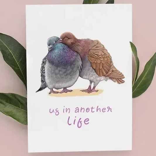 Illustration of two pigeons hugging with text 'us in another life' on a pink background with leaves.