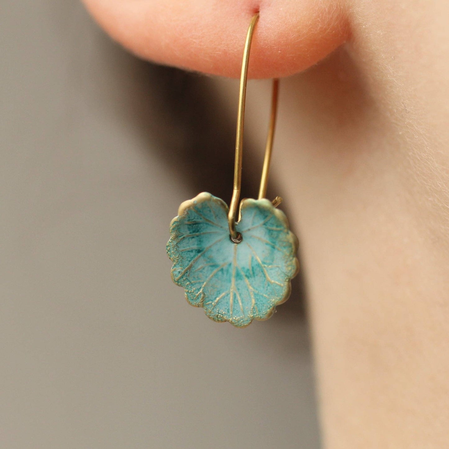 Gold earring with a turquoise stone worn on an ear against a neutral background