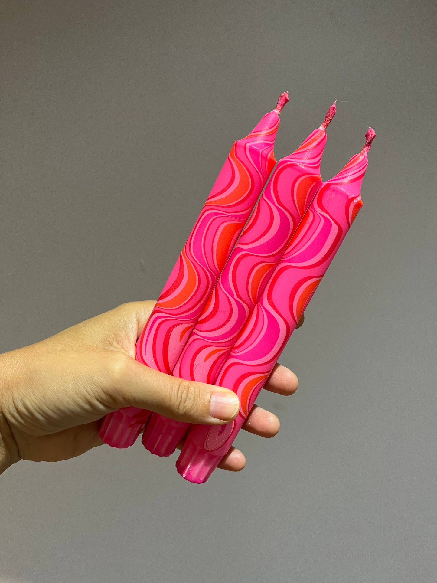 Hand holding pink wavy-patterned candles against a gray background