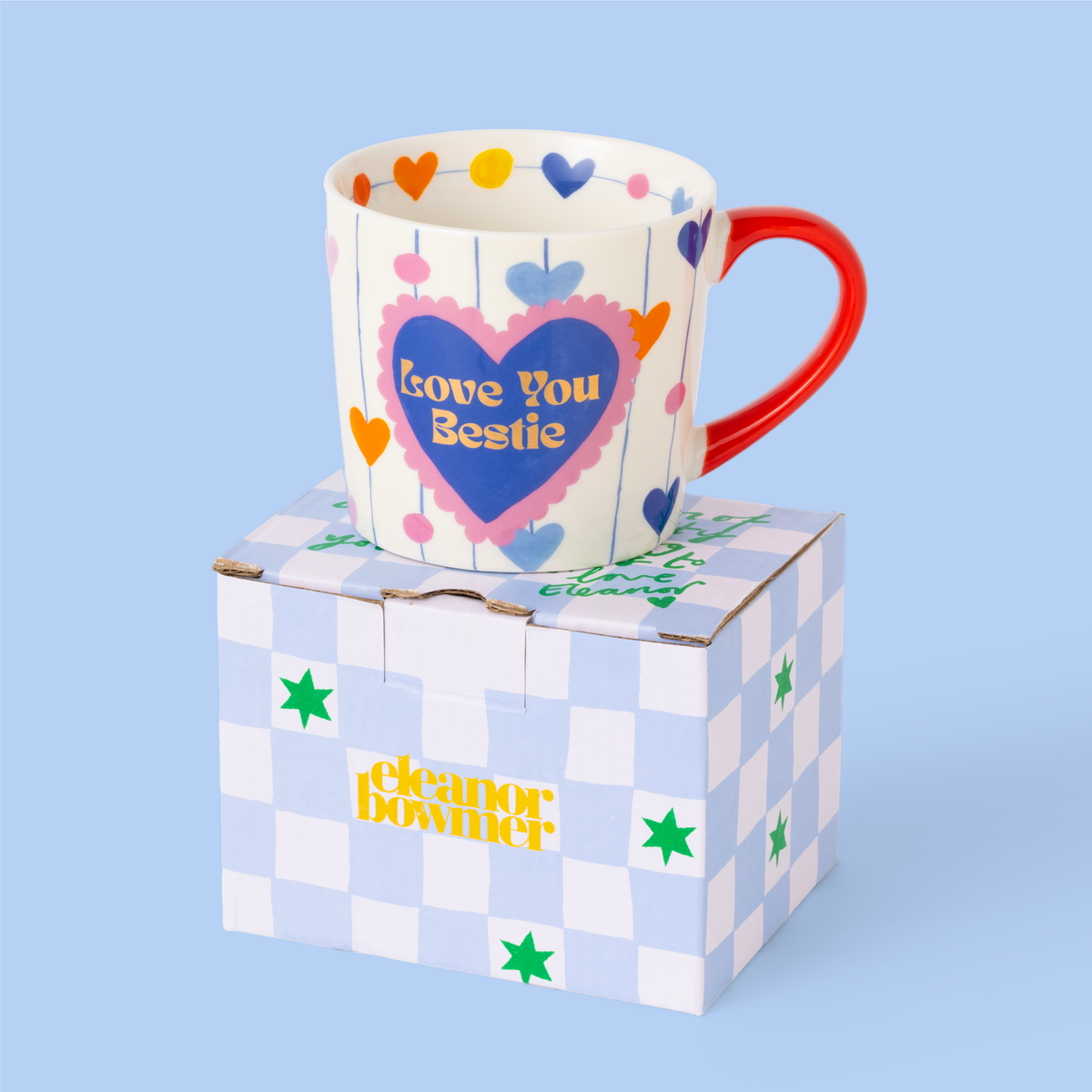 Colorful mug with heart design and 'Love You Bestie' text on a checkered box against a light blue background.