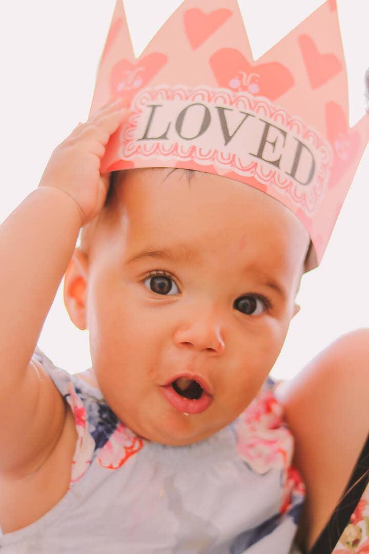 Baby wearing a pink crown with 'LOVED' text against a light background