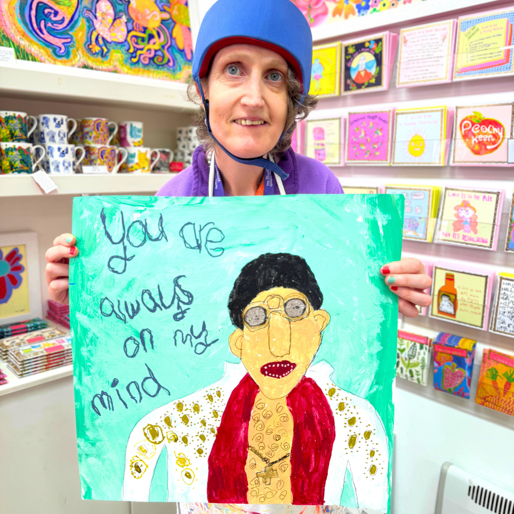 Person holding a colorful painting of a person with text in a store setting