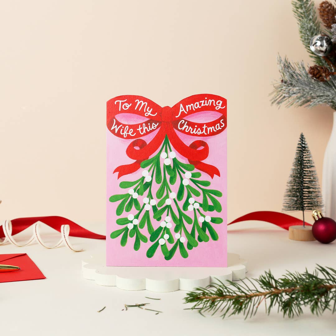 Christmas card. Text is To my amazing wife this Christmas. Illustrations of a bunch of mistletoe with a big red ribbon.