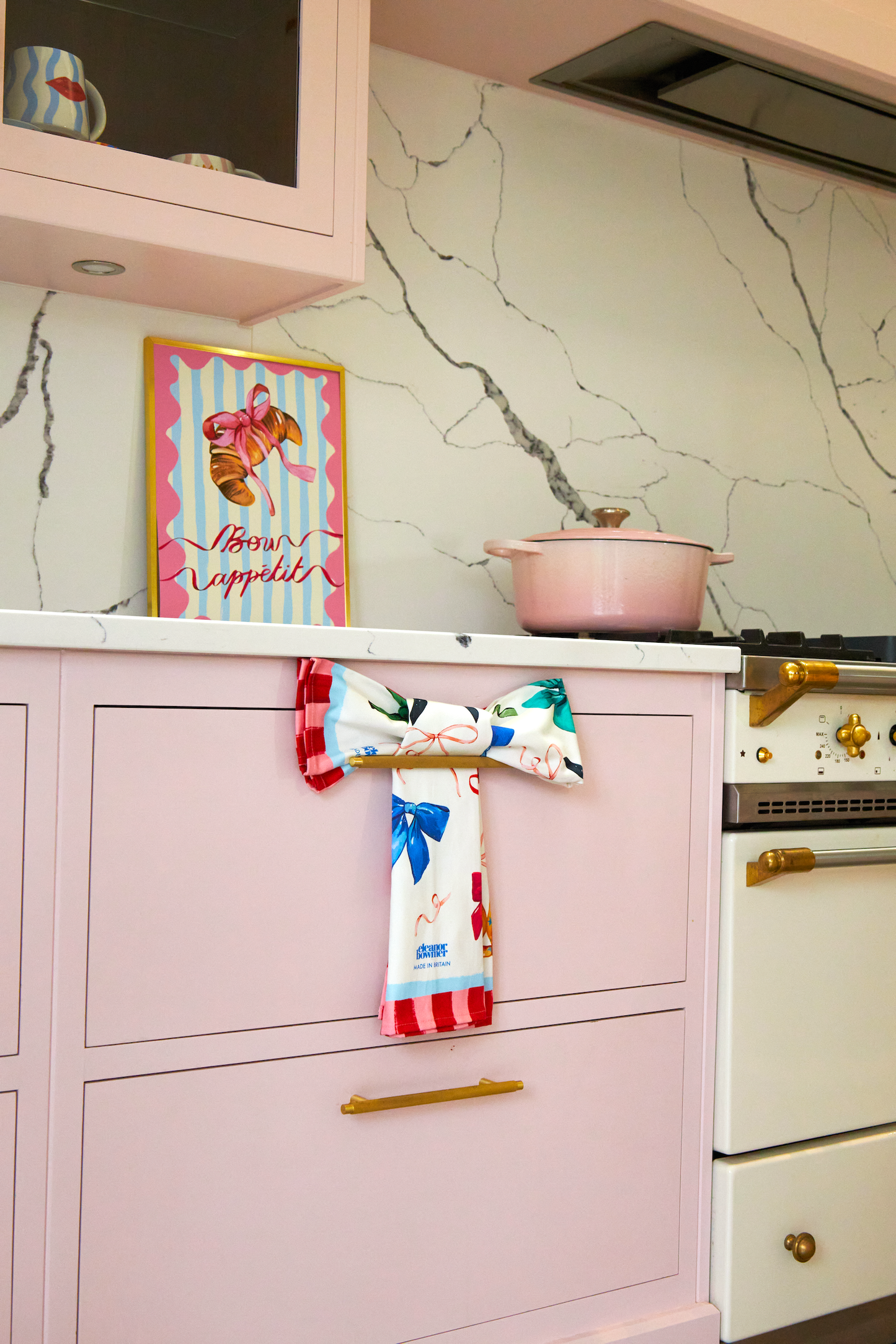 Kitchen with pink cabinets, marble backsplash, and colorful towels hanging on a handle.