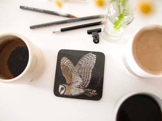 A square black coaster with rounded corners featuring a detailed illustration of a barn owl in flight.