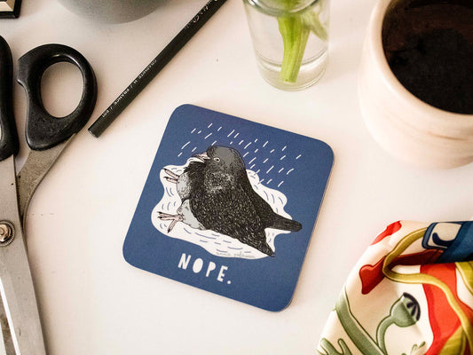 A square blue coaster with a pigeon illustration sitting in a puddle with the word 'NOPE.' underneath.