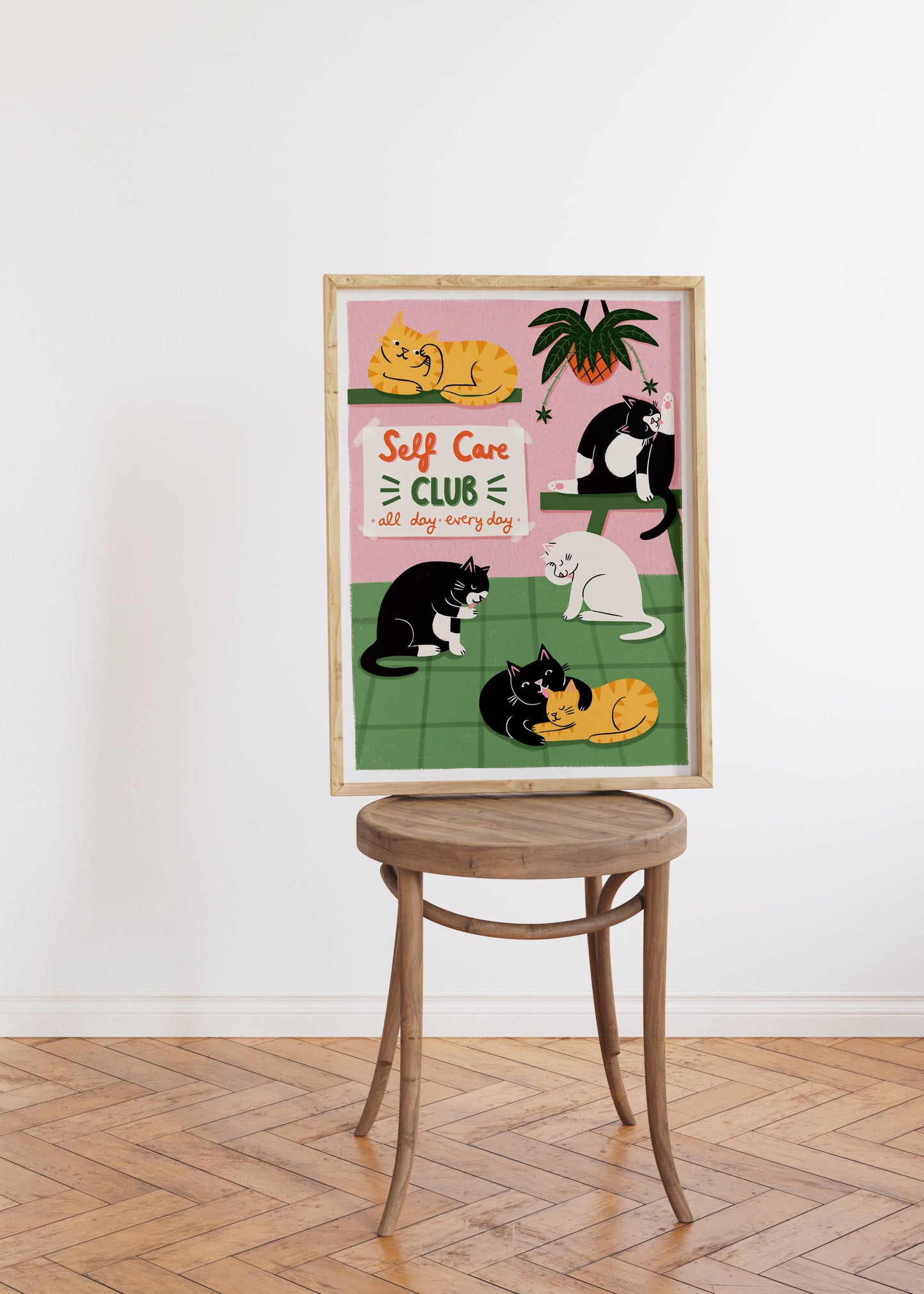 Framed artwork with cats and 'Self Care Club' text on a white wall.