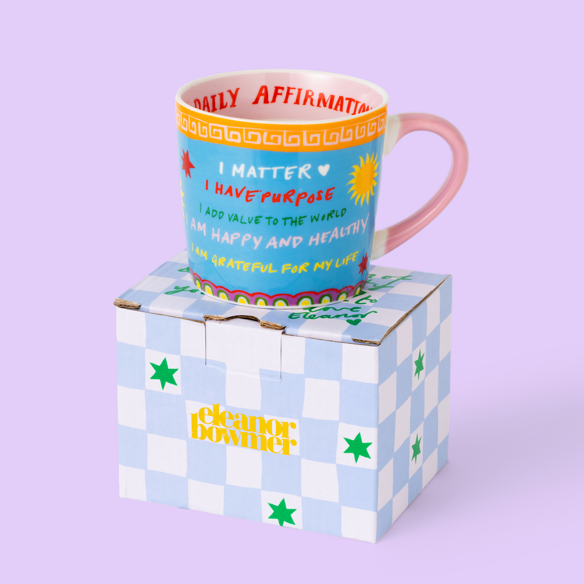Colorful mug with motivational text on a checkered box against a light purple background