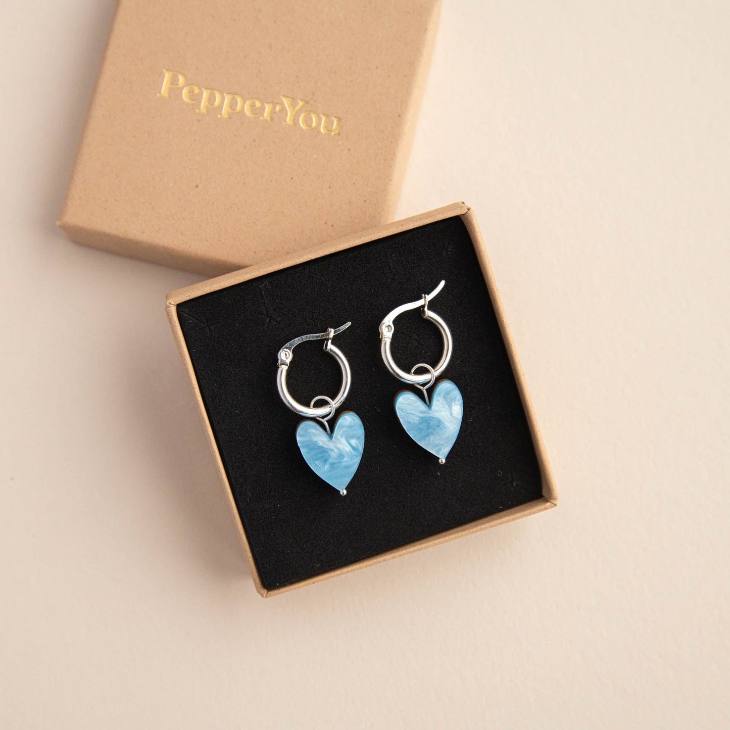 Heart-shaped earrings in a 'PepperYou' branded box on a beige background