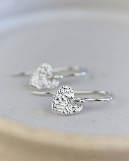 Silver heart-shaped earrings on a light gray background