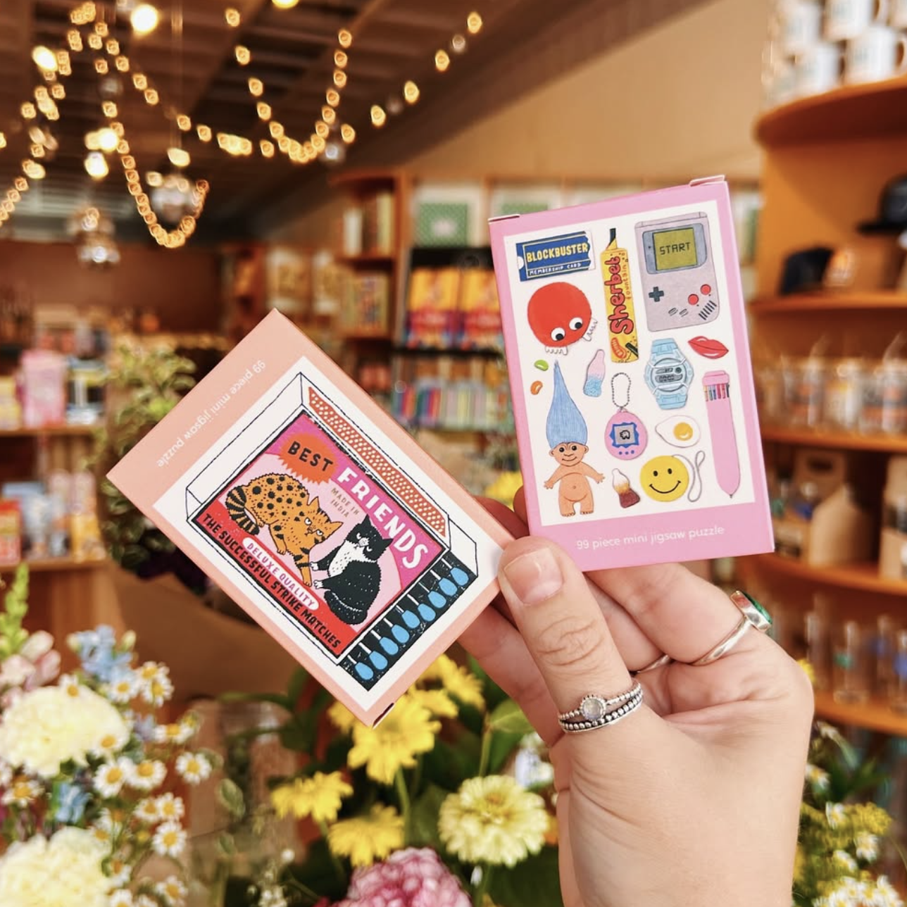 Two small packages with colorful designs held in a hand against a store background.
