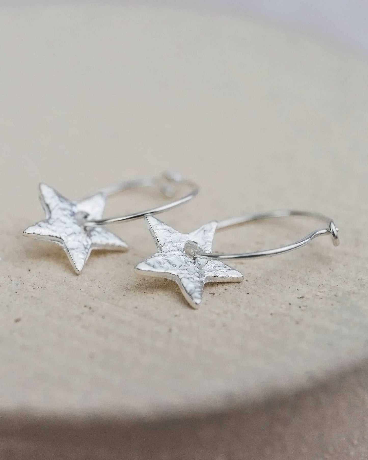 Silver star-shaped earrings on a beige surface
