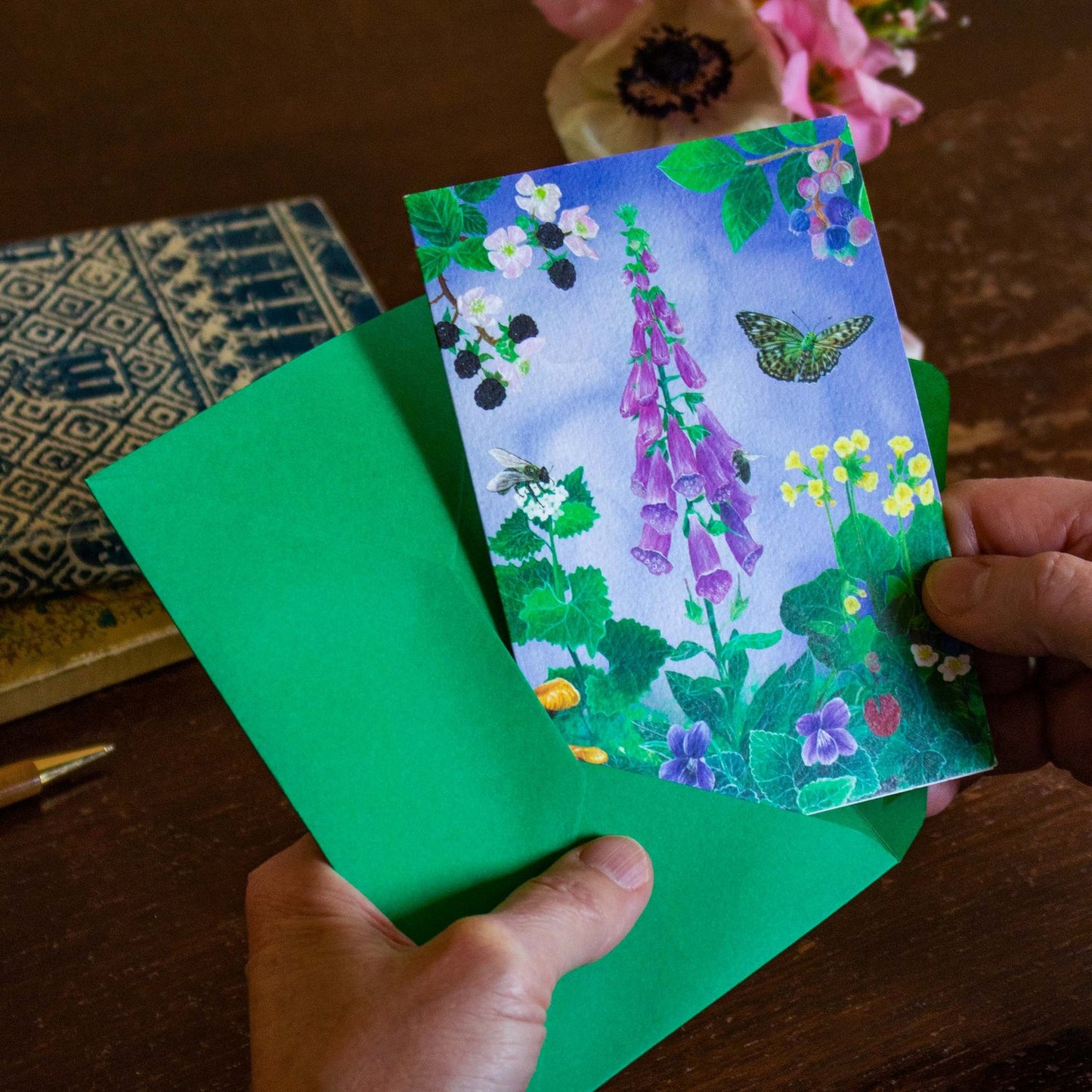 This card features a busy woodland floor scene of hand-painted acrylic illustrations. It includes a tall pink foxglove, wild strawberries and many bees, butterflies and crawlers. The pale blue-lilac watercolour background adds more depth to the scene. Around the foxglove, violets and cowslips you can spot a bright yellow Brimstone Butterfly, a large speckled Fritillary Butterfly and even a snail peaking through the leaves. The card is fully printed back to front and is like a little piece of art.