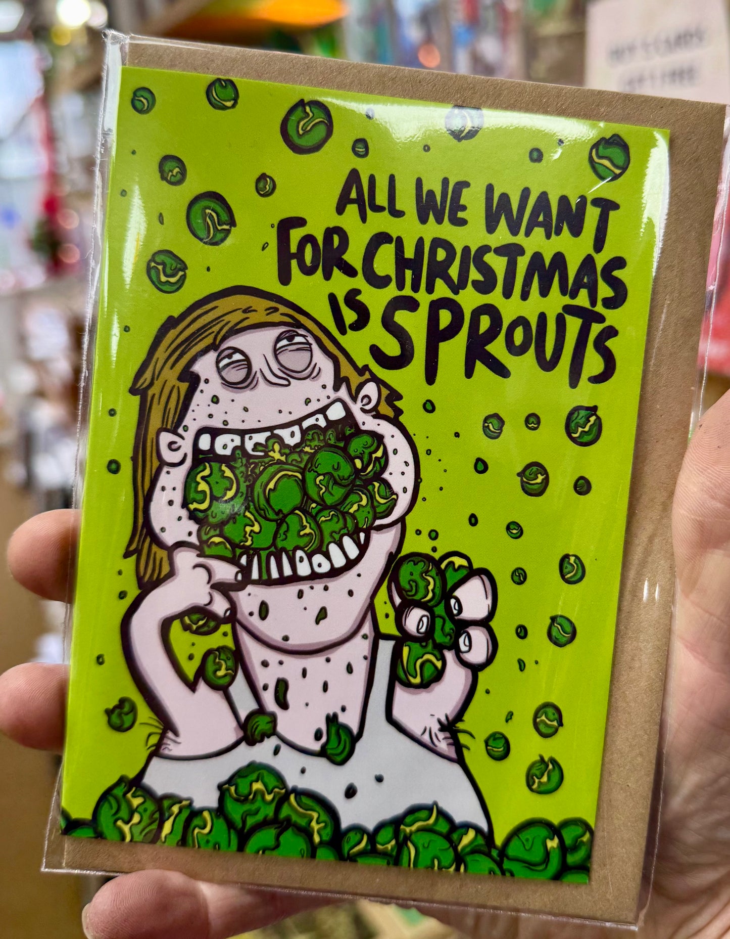 All we want for Christmas is Sprouts card. A man in a vest top devouring a large amount of sprouts!