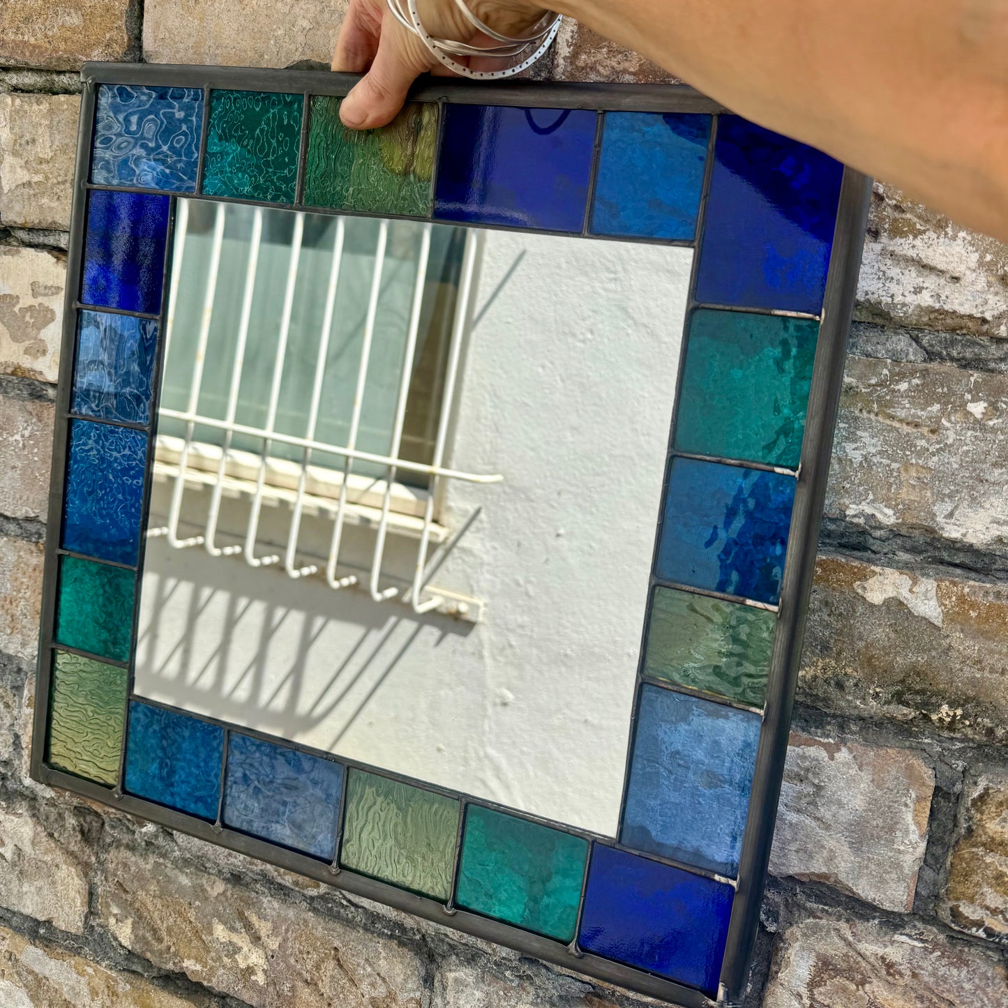 Square stained glass mirror with a 6cm border of greens, blues and aqua colours.