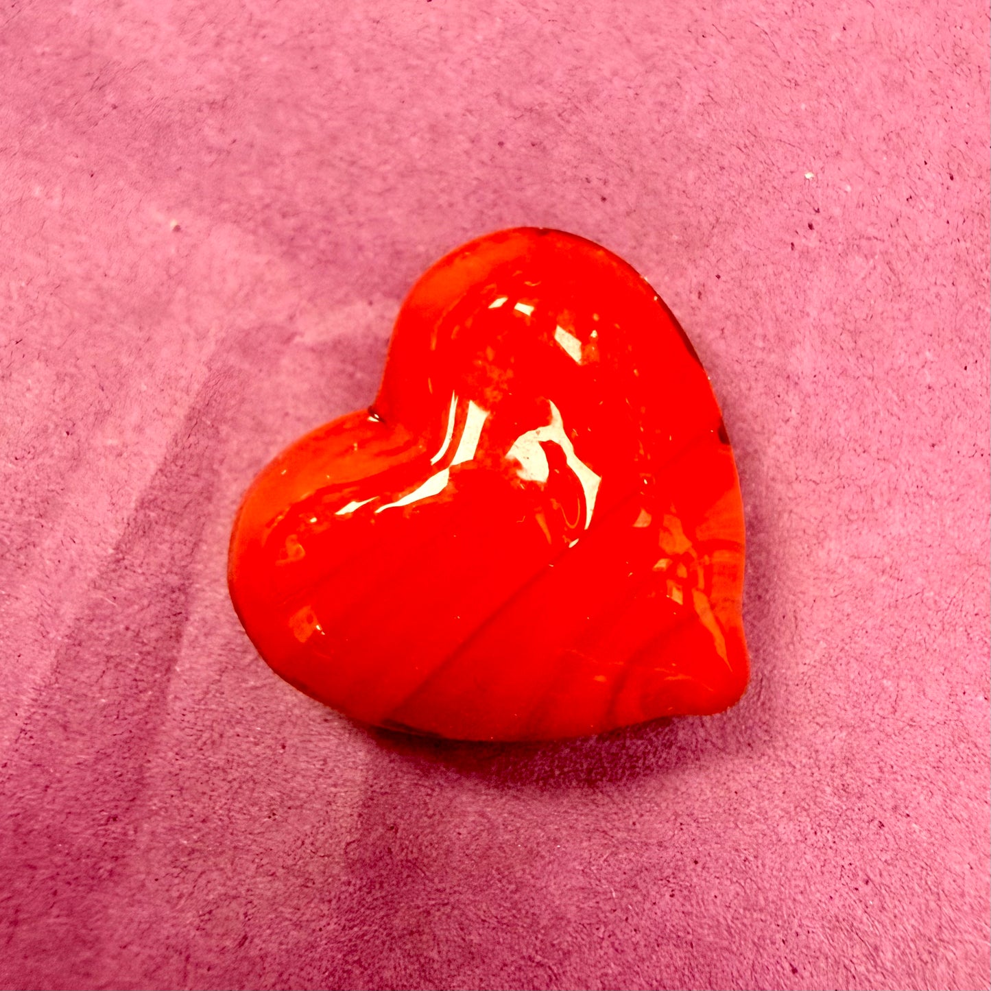 A glossy, heart-shaped red wax seal or stamp resting on a textured pink paper background.