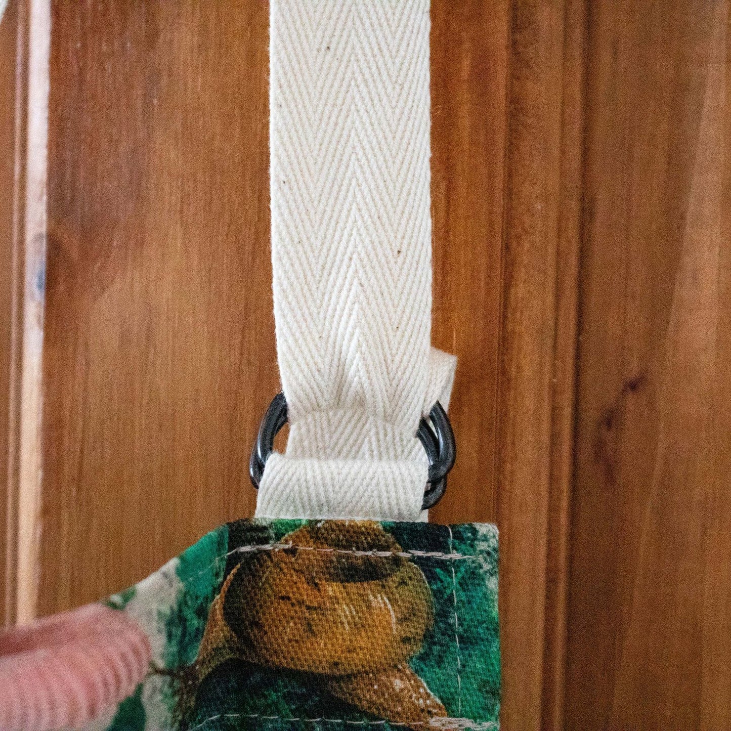 A Close up view of an adjustable D Ring fastening of an apron with a cream strap.