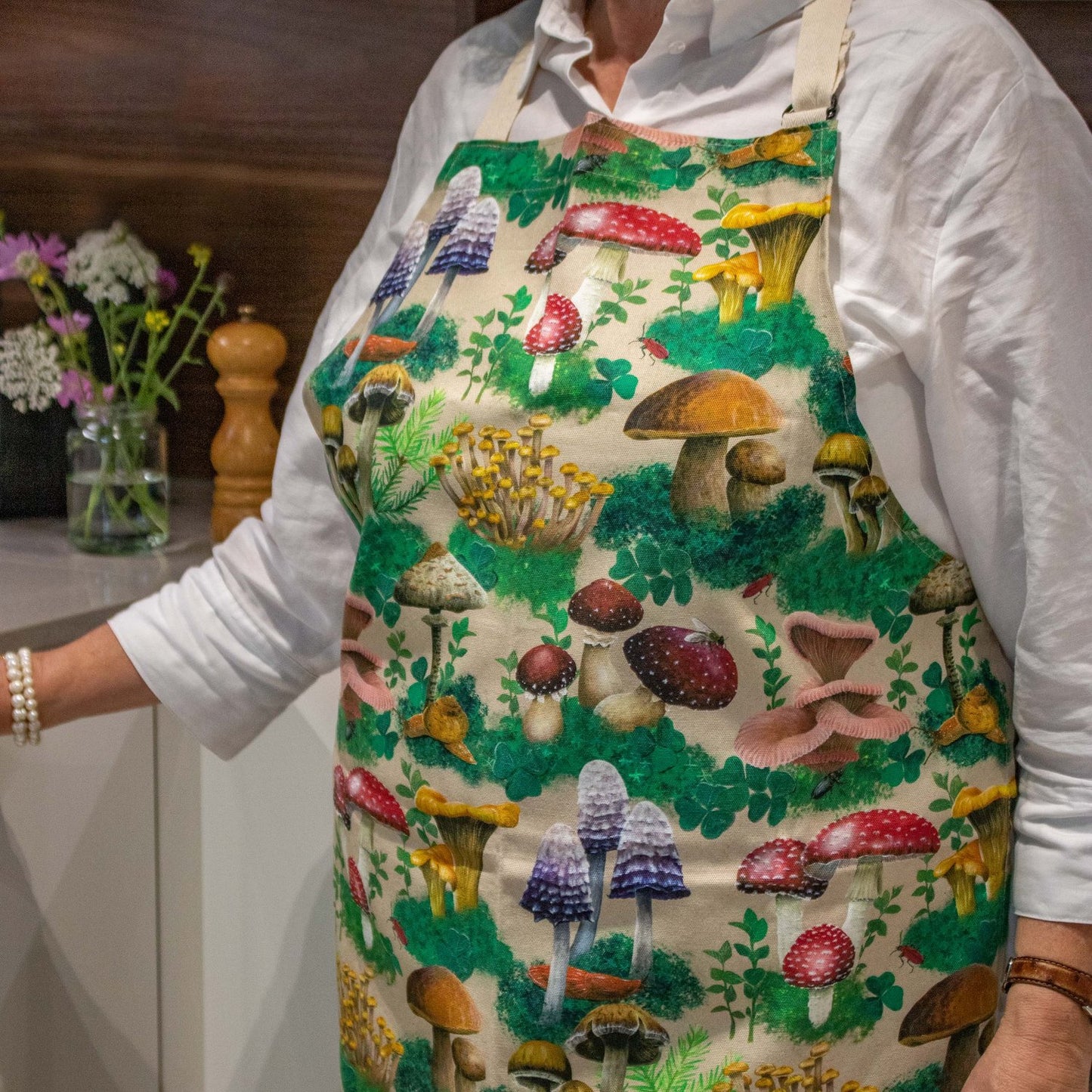 A close up view of a person's torso wearing an apron with a design made up of a variety of woodland mushrooms and moss.
