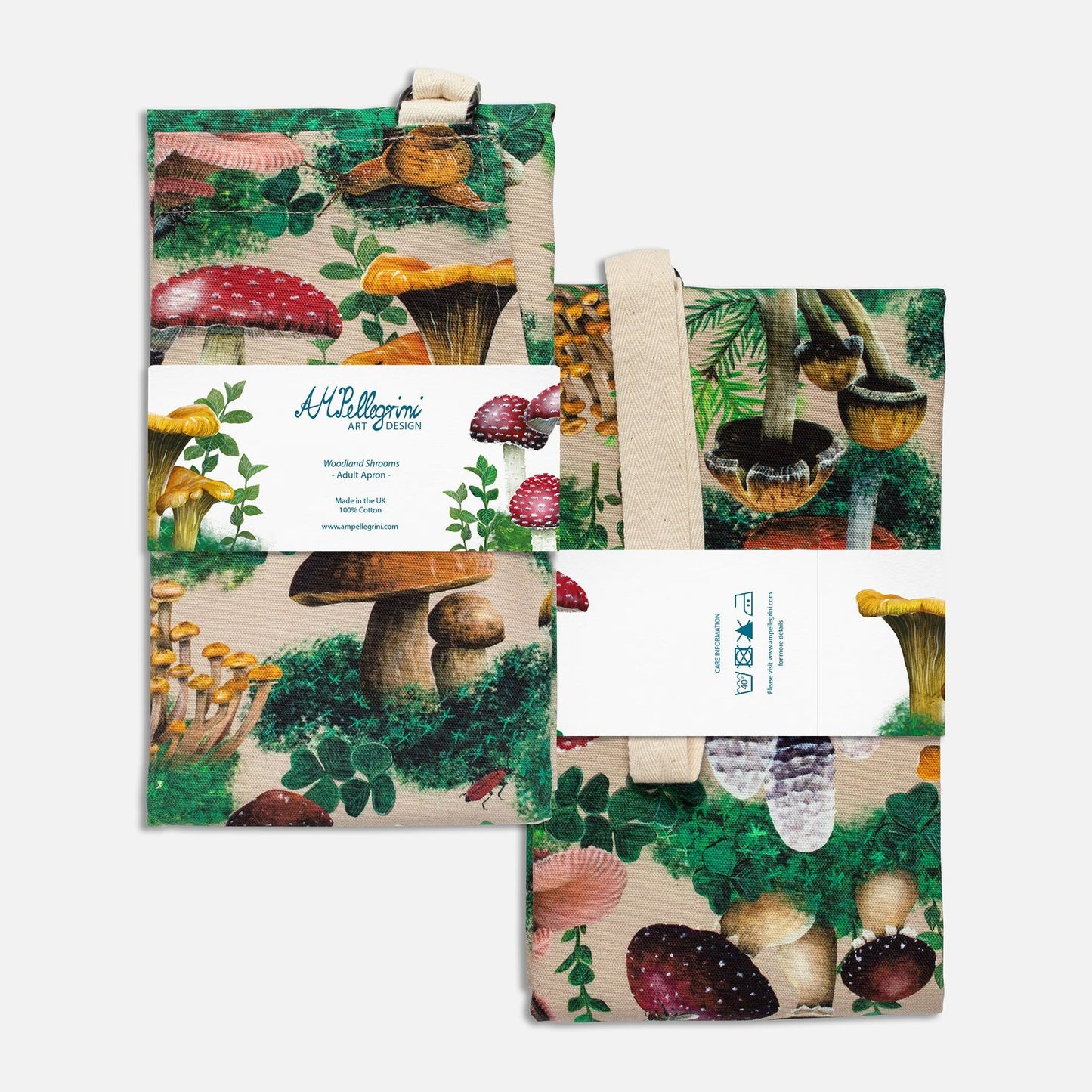 An image of the front and back of a packaged, folded apron with a woodland mushroom print. The apron is packaged with a paper band displaying the artist's logo and product description (front) and care instructions (back).