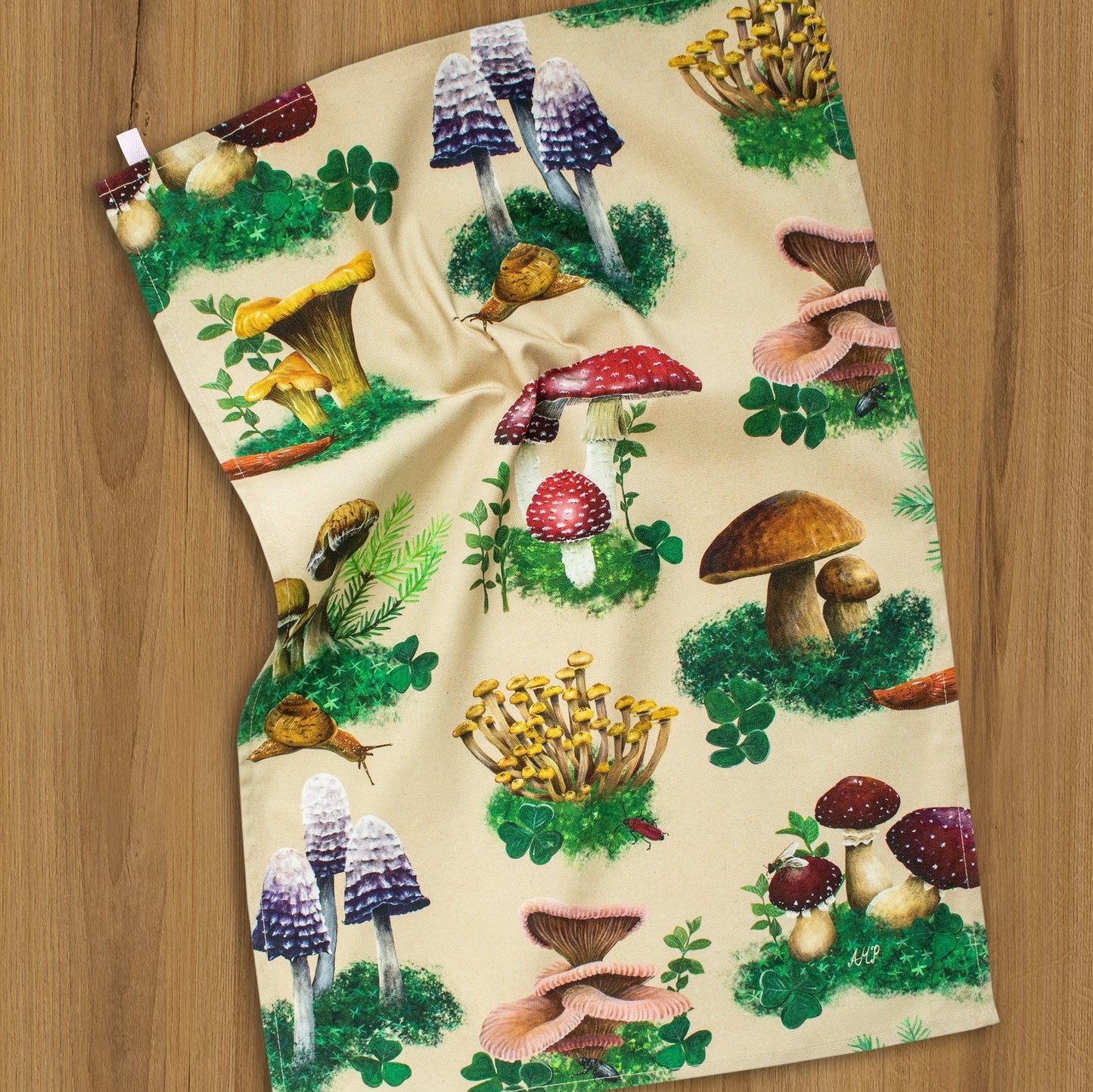 An outstretched tea towel depicting a print of various woodland mushrooms.