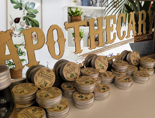 Collection of apothecary jars with decorative labels on a table, featuring a large 'Apothecary' sign in the background.