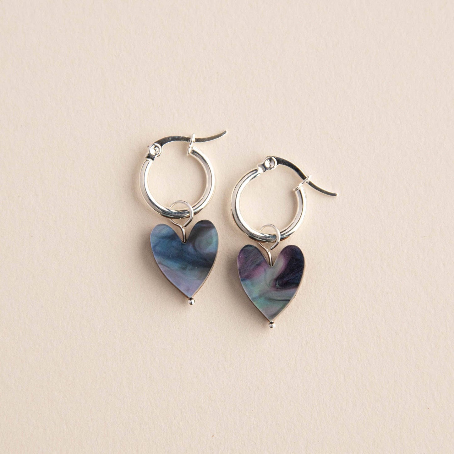 Silver hoop earrings with heart-shaped multicolored charms on a beige background