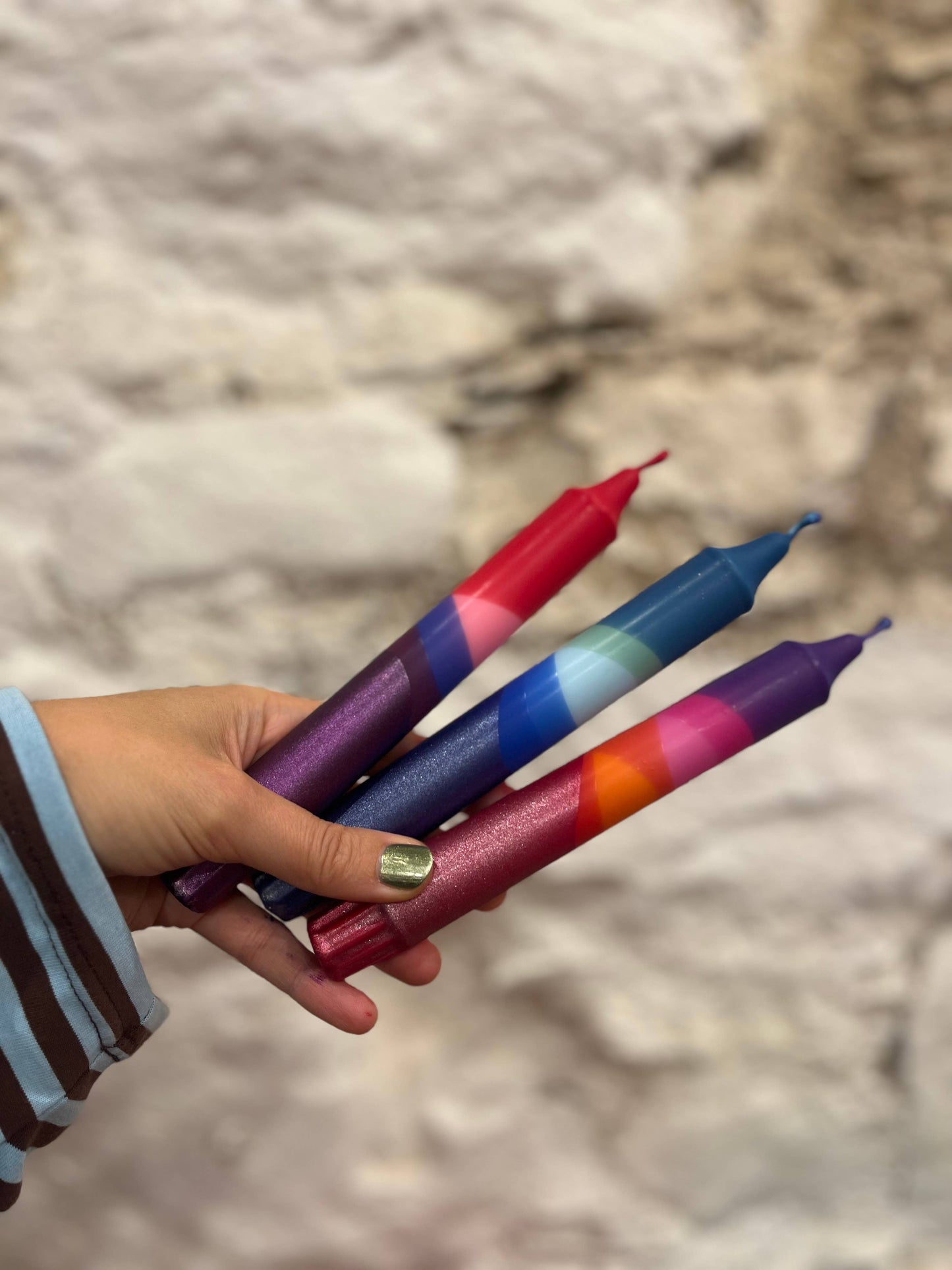 Hand holding four colorful markers against a stone wall background