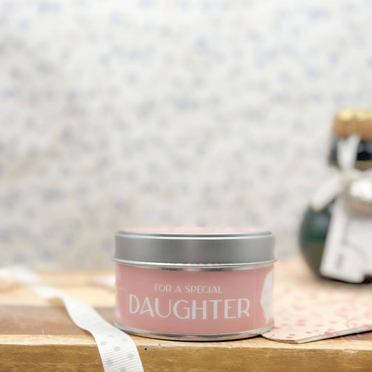 Candle in a tin labeled 'For a Special Daughter' on a wooden surface with a blurred background.