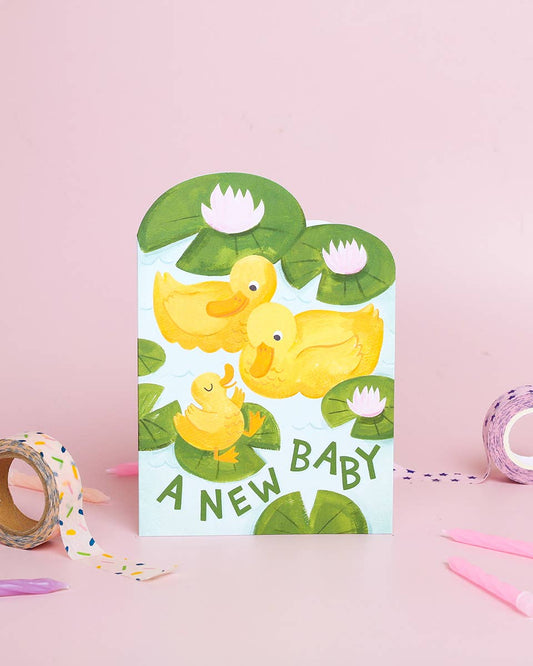 Greeting card with yellow ducks and 'A New Baby' text on a pink background